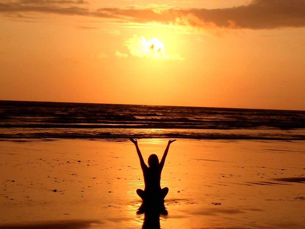 Frau sitzt am Strand bei einem Sonnenuntergang